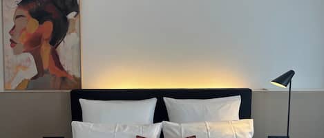 Une chambre d’hôtel avec un lit, des oreillers, un tableau au mur et une lampe sur pied.