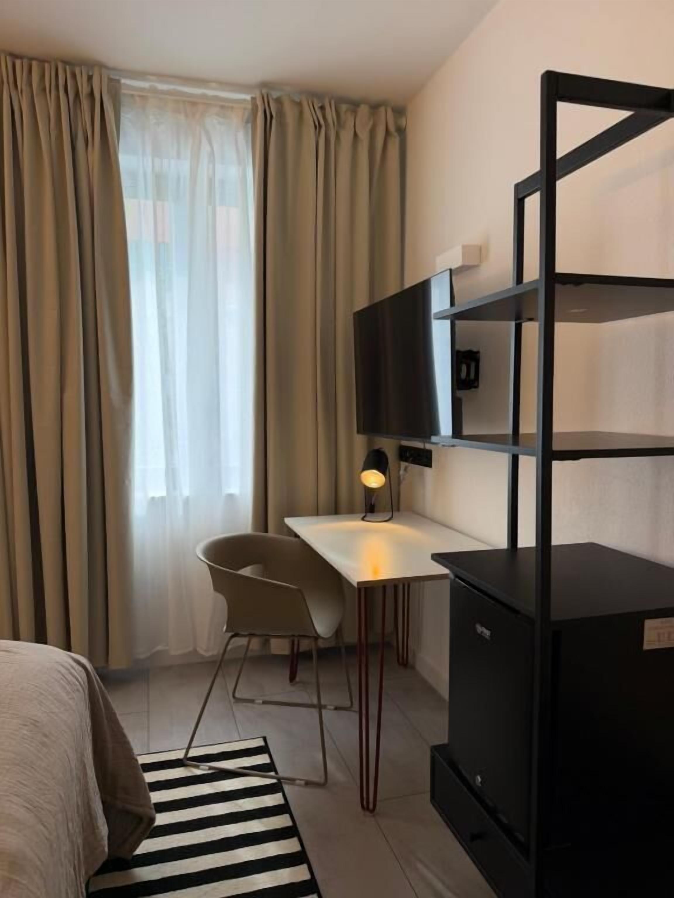 A compact hotel room with a bed, a desk, a chair, a television, and a wardrobe.
