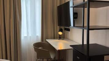 A compact hotel room with a bed, a desk, a chair, a television, and a wardrobe.