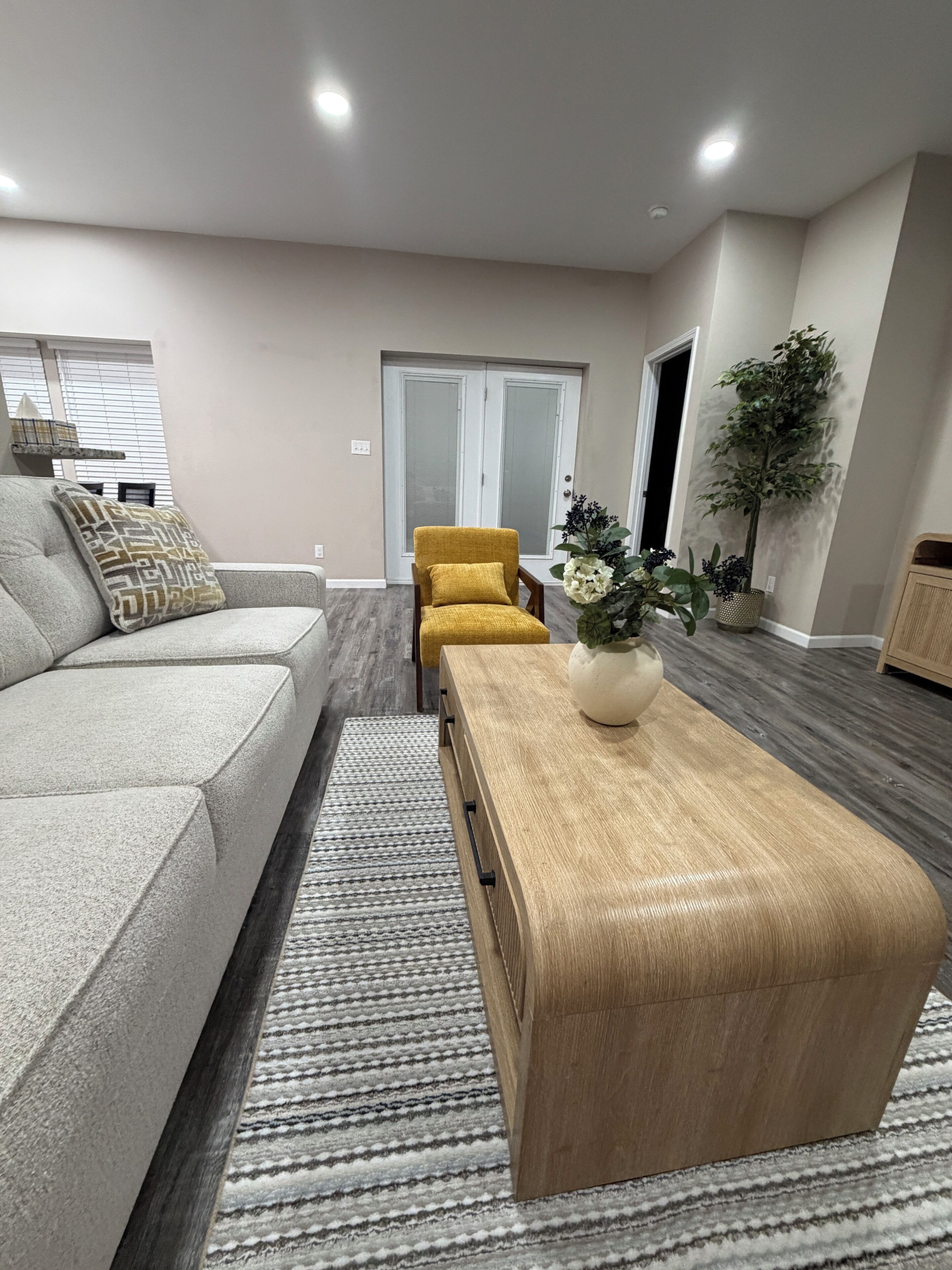 A modern living room with a sofa, a wooden coffee table, and a yellow armchair.
