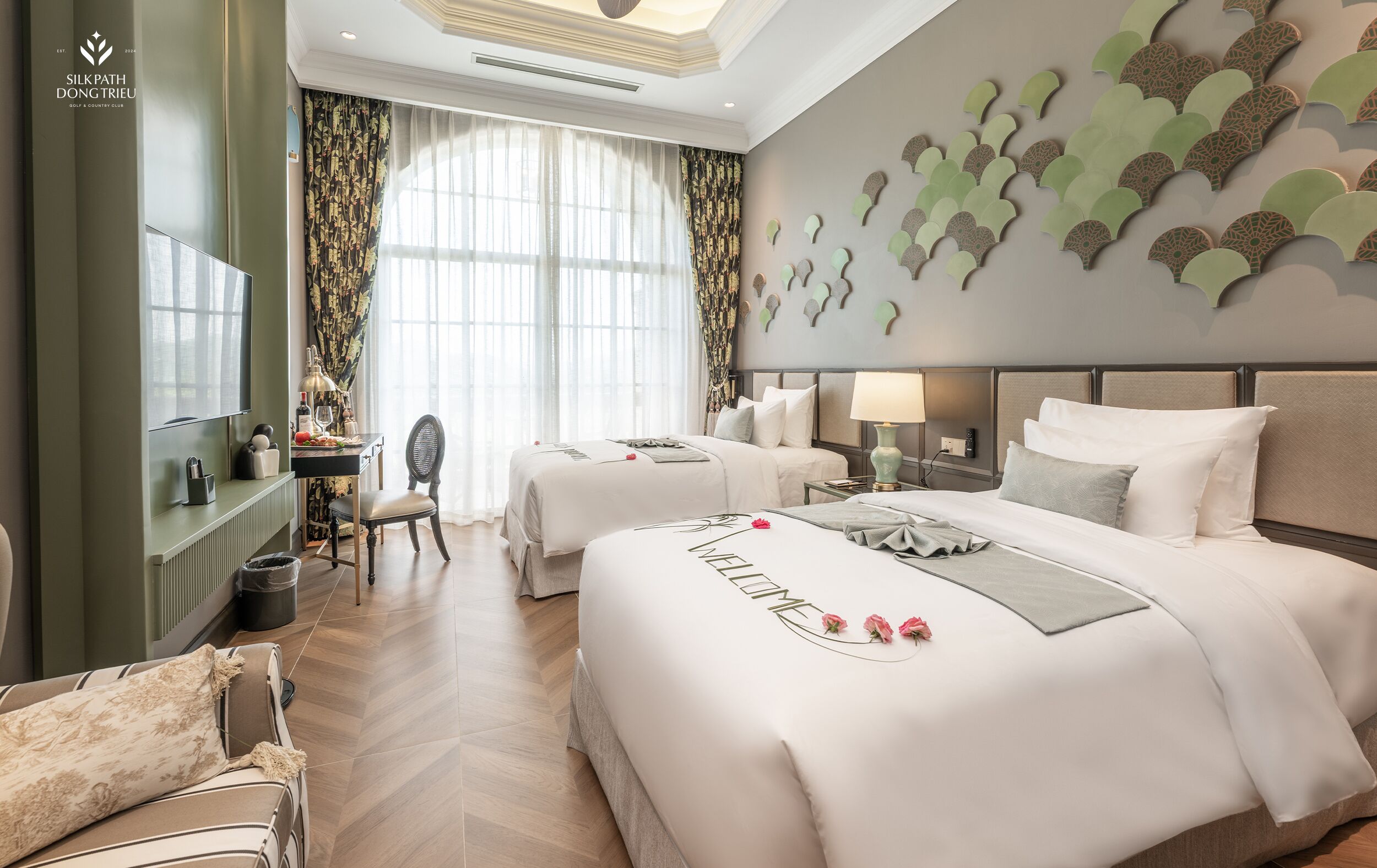 Une chambre d’hôtel avec deux lits, un bureau, une chaise et une grande fenêtre avec des rideaux.