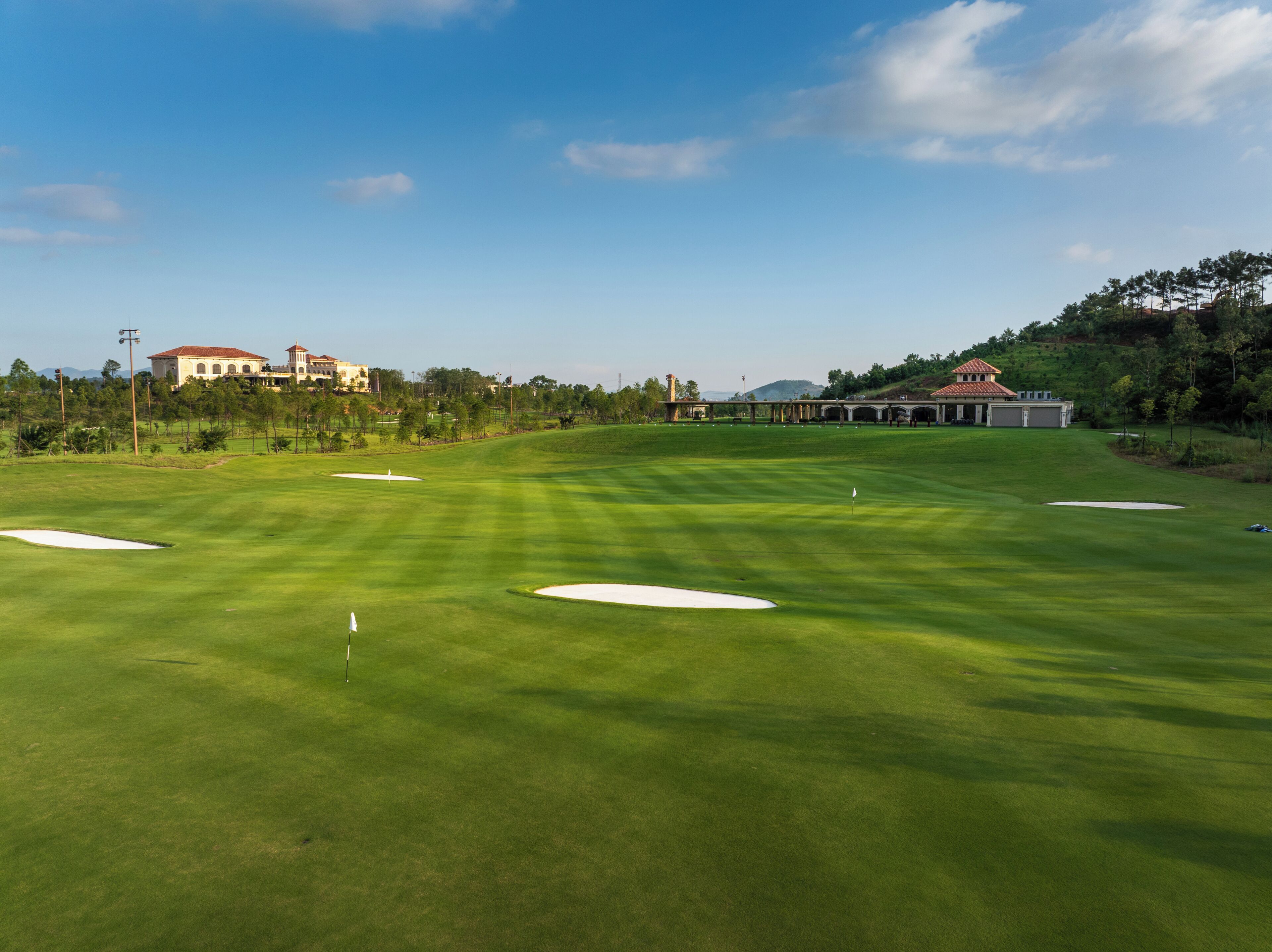 A golf course with sand bunkers, a flag, and a clubhouse in the background.