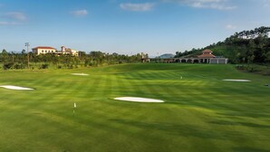 A golf course with sand bunkers, a flag, and a clubhouse in the background.