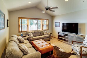 A living room with a sectional sofa, a leather ottoman, a television on a wooden stand, and a ceiling fan.
