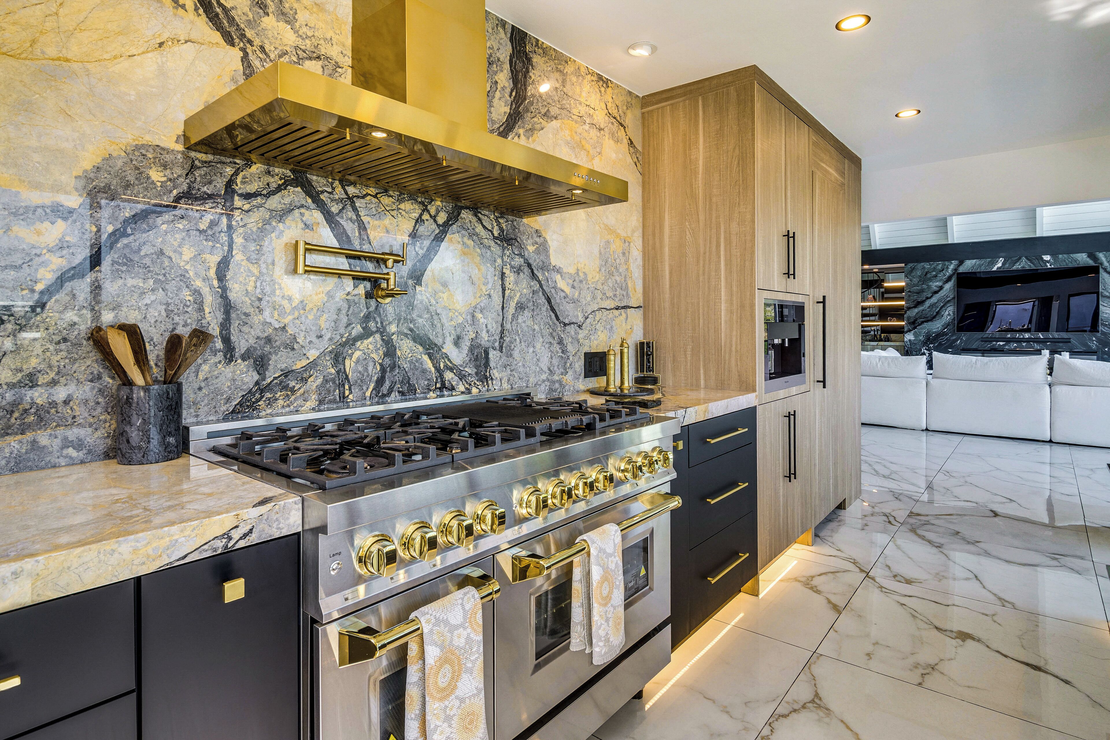 A modern kitchen with a gas stove, oven, and marble backsplash.