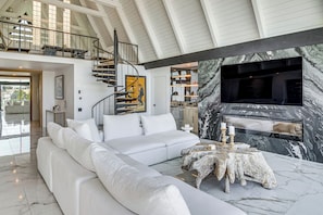 A spacious living area with a white sofa, a marble fireplace, and a modern staircase.