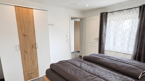 Een slaapkamer met een bed, een kledingkast en een raam met gordijnen.