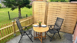 Een terras met een ronde houten tafel, twee zwarte stoelen en een kleine plant in een pot.