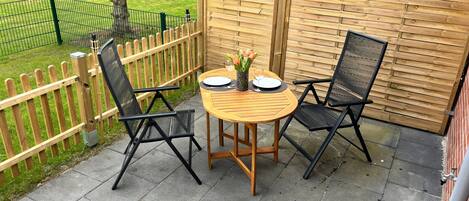 A patio with a round wooden table, two black chairs, and a small potted plant.