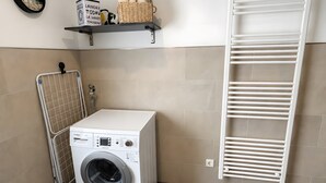 Een wasruimte met een wasmachine, een droogrek en een plank met handdoeken en een wasmand.