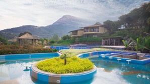 Una piscina con una isla central, rodeada por un jardín ajardinado y una montaña al fondo.