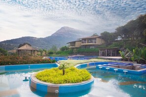 Una piscina con una isla central, rodeada por un jardín ajardinado y una montaña al fondo.