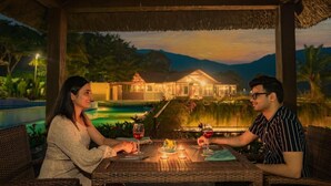 Una pareja cenando en una mesa al aire libre con vistas a un complejo turístico y montañas al fondo.