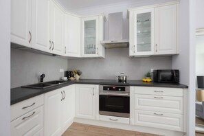 A modern kitchen with white cabinetry, a black countertop, a built-in oven, and a microwave. - Comfortable Apartment with a Balcony  Near the Airport (Warsaw)