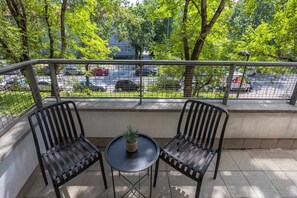 A balcony with two chairs and a small table, overlooking a parking area and trees. - Comfortable Apartment with a Balcony  Near the Airport (Warsaw)