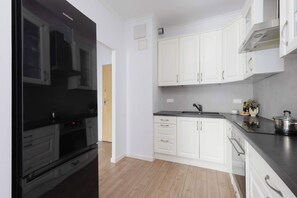 A modern kitchen with white cabinets, a black refrigerator, and a stainless steel range hood. - Comfortable Apartment with a Balcony  Near the Airport (Warsaw)
