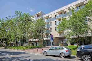 A modern building with a parking sign, trees, and a white car parked in front. - Comfortable Apartment with a Balcony  Near the Airport (Warsaw)