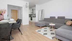Een moderne woonkamer met een grijze modulaire bank, een eethoek met een tafel en stoelen, en een keuken op de achtergrond.
