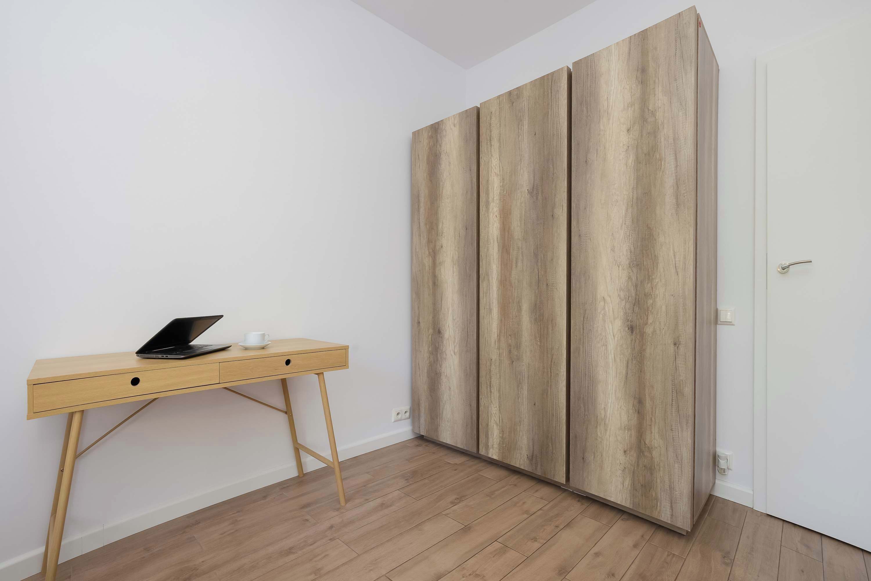 Een kamer met een houten bureau, een laptop en een garderobe met een houtnerf afwerking.