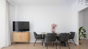 Een moderne eethoek met een houten kast, een flatscreen televisie, een tafel gedekt voor vier personen en een kamerplant.