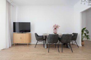 A modern dining area with a wooden cabinet, a flat-screen TV, a table set for four, and a potted plant. - Comfortable Apartment with a Balcony  Near the Airport (Warsaw)