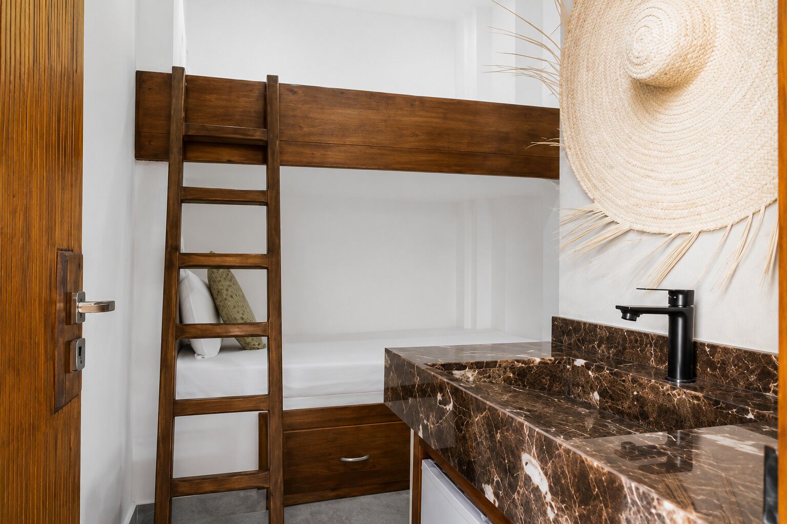 A bathroom with a wooden ladder, a marble sink, and a large woven hat hanging on the wall.