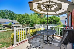 Une terrasse avec une table et des chaises, un grand parasol et une clôture blanche.