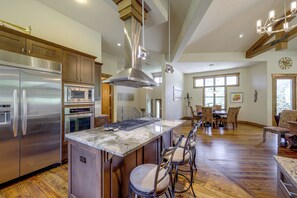 A spacious kitchen with a large island, stainless steel appliances, and a dining area with wooden flooring and patterned chairs. - Stunning Eagle-Vail Escape! Mtn Views + Deck (Avon)