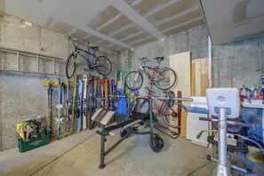 Uma garagem com bicicletas, esquis e um banco de musculação.
