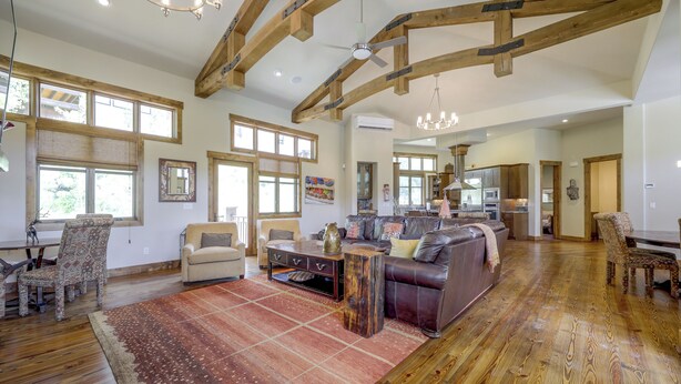 A spacious living area with a large wooden beam ceiling, a fireplace, and a dining area with a wooden table and chairs. - Stunning Eagle-Vail Escape! Mtn Views + Deck (Avon)
