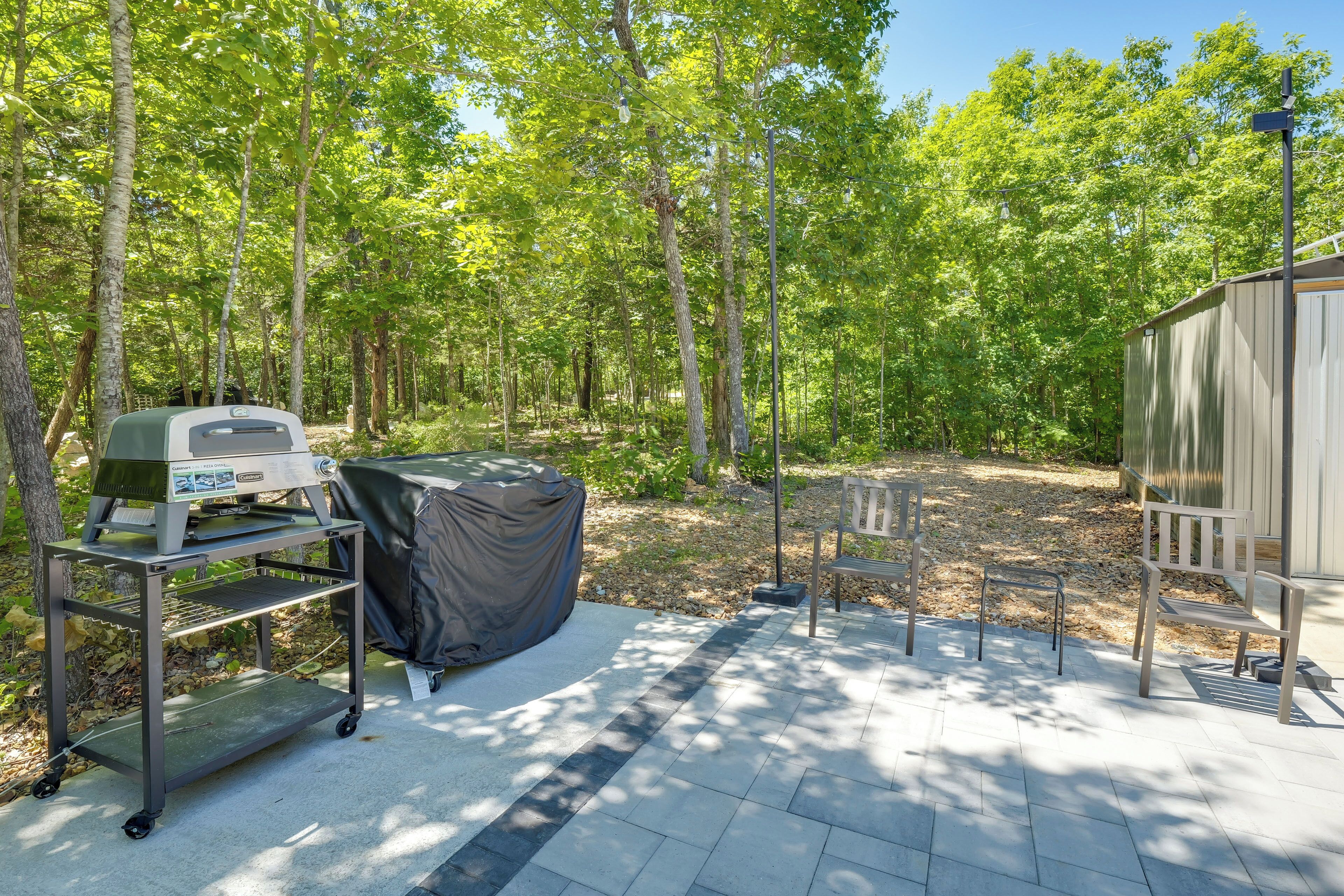 A patio area with a grill, a covered table, a bench, and a shed.