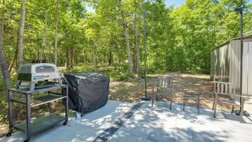 A patio area with a grill, a covered table, a bench, and a shed.
