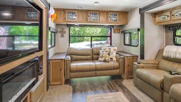 A well-equipped RV interior with a leather sofa, a television, and wooden cabinets.