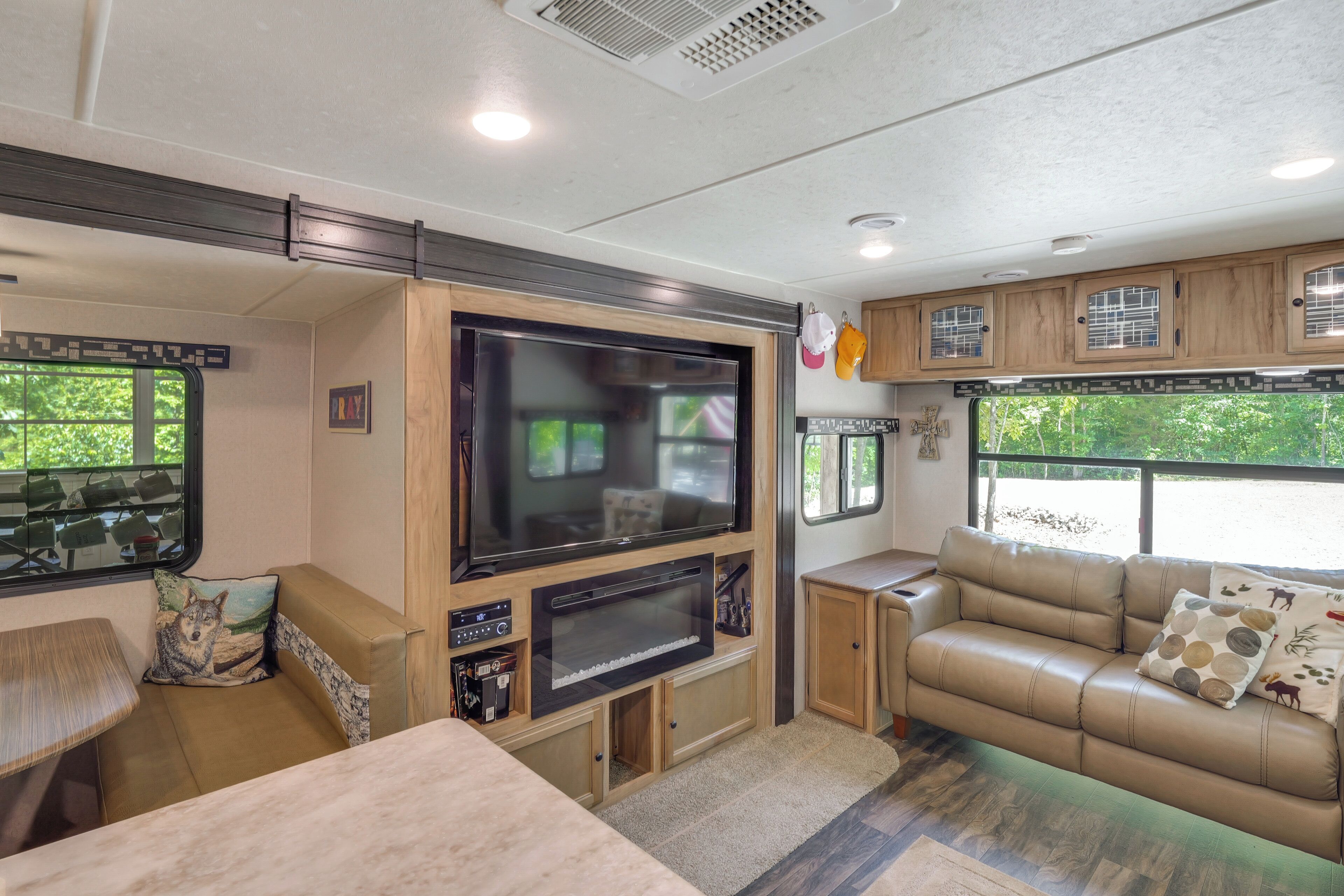 A well-lit RV interior with a large flat-screen TV, a sofa, and a dining area.
