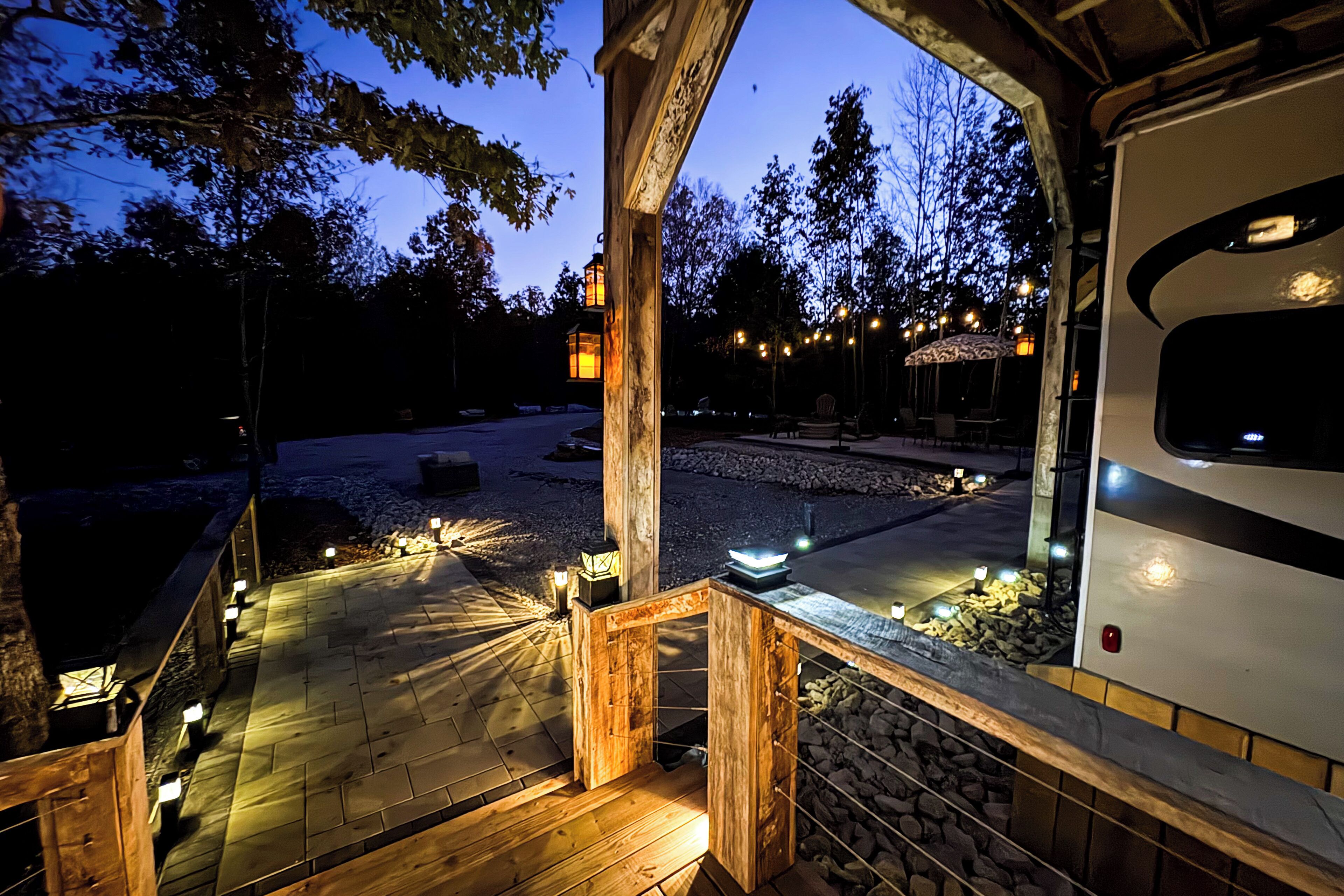 A wooden deck with outdoor lighting, a covered seating area, and a view of a vehicle.