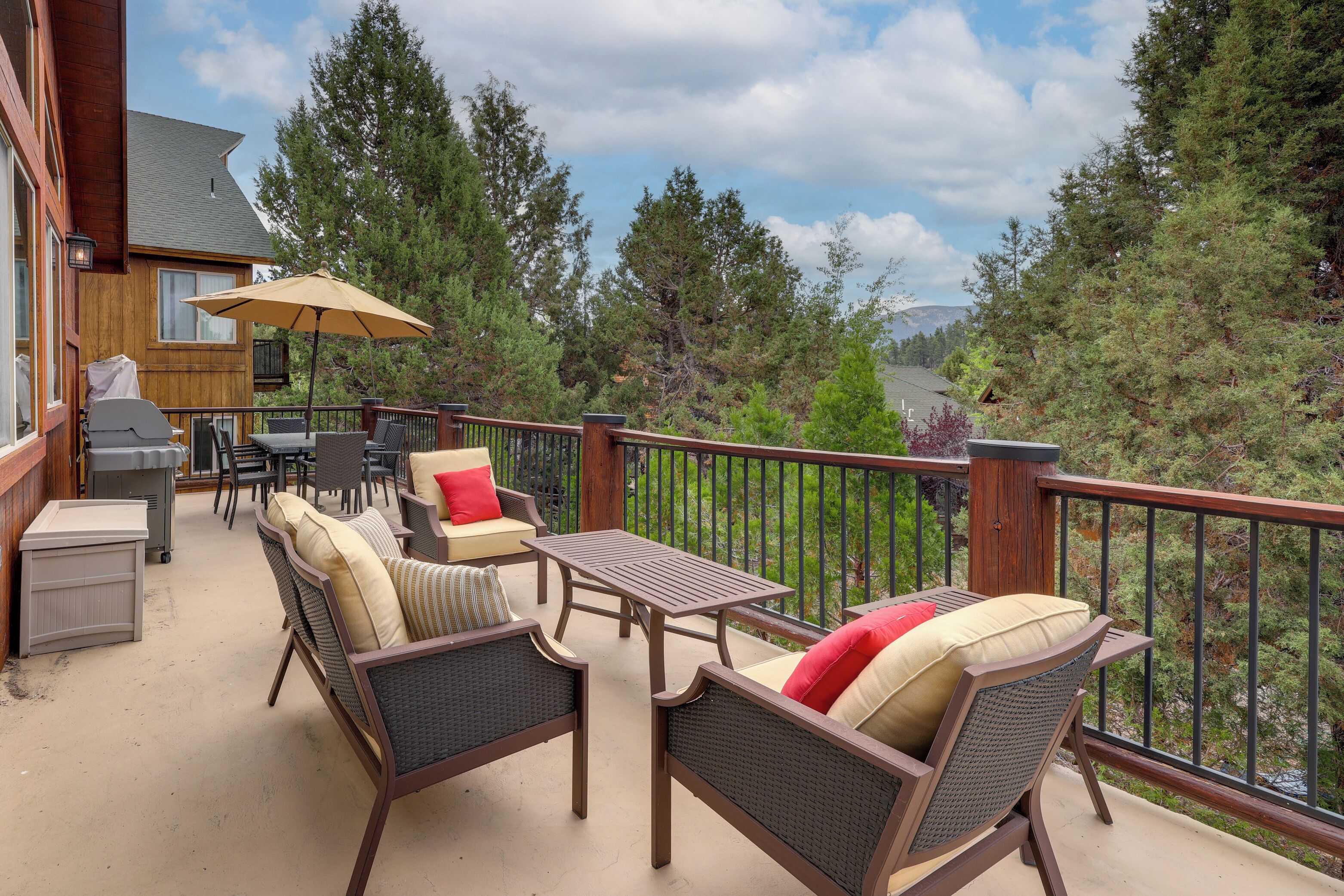 Une terrasse extérieure couverte, aménagée avec des meubles en osier, un barbecue et offrant une vue sur les arbres et les montagnes.