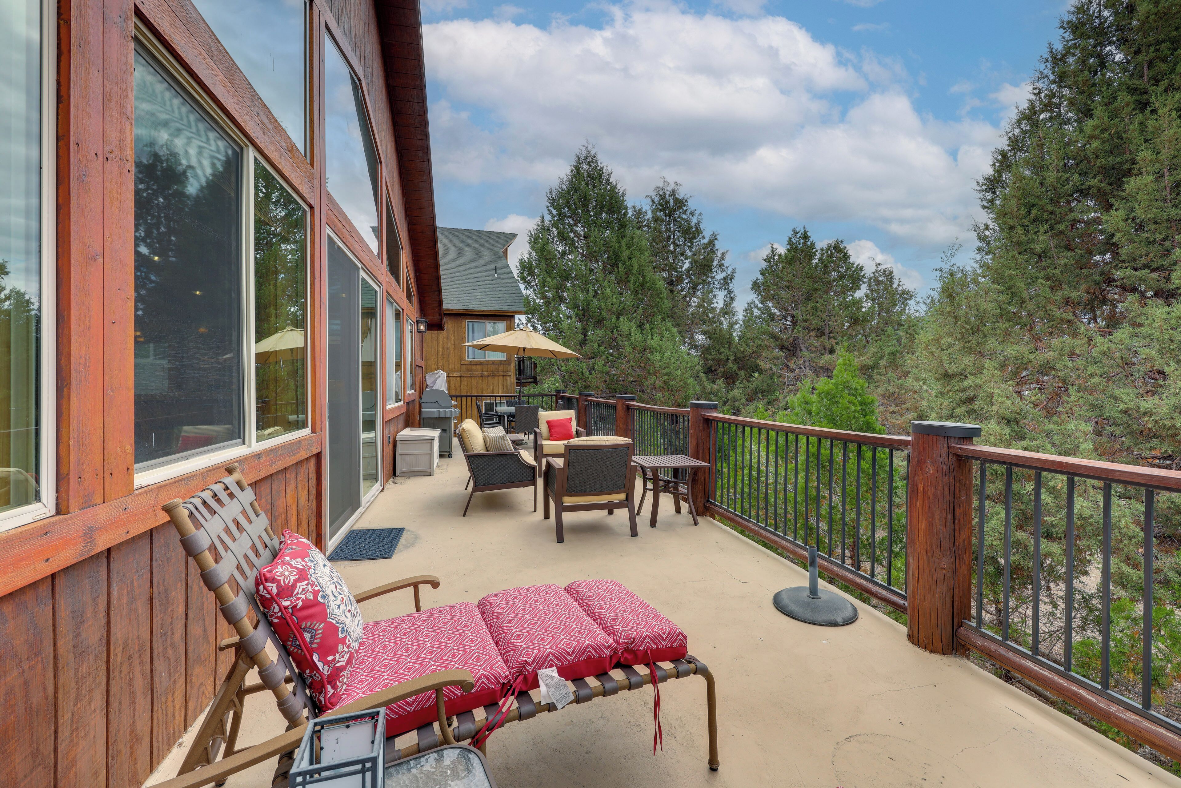 A wooden deck with outdoor furniture, including a bench and chairs, overlooking a forested area.