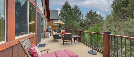 Une terrasse en bois, aménagée avec du mobilier d’extérieur, notamment un banc et des chaises, donnant sur une zone boisée.