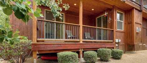 Una construcción de madera con un porche cubierto, una silla roja y un pequeño jardín con arbustos.