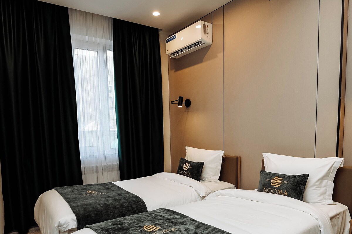 Habitación de hotel con dos camas, un ventanal con cortinas, un aire acondicionado y una lámpara fijada a la pared.
