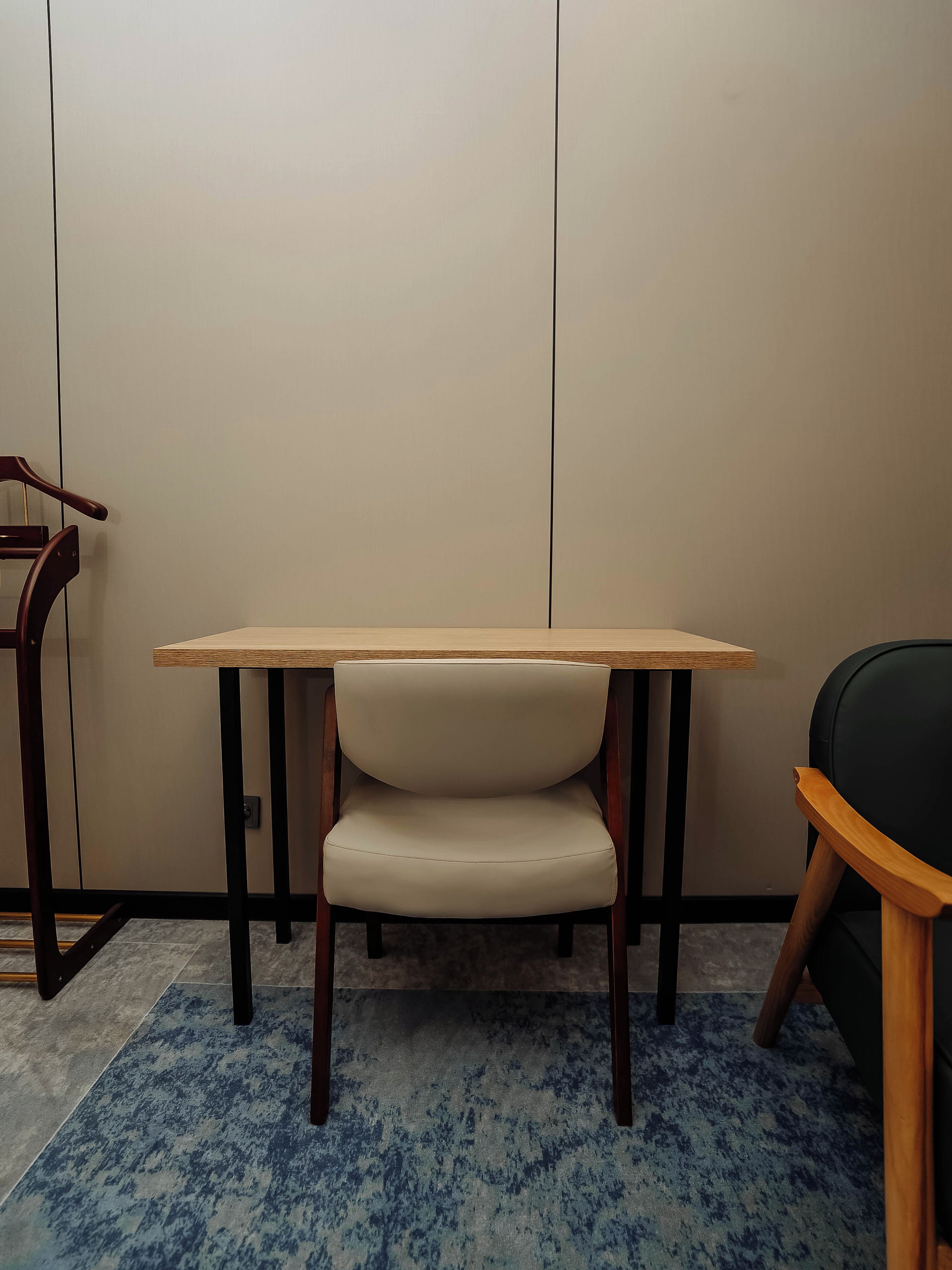 A room with a wooden table, a chair with a cushioned seat, and a blue patterned carpet.