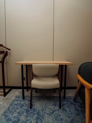 Una habitación con una mesa de madera, una silla con asiento acolchado y una alfombra azul estampada.