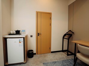 Una cocina compacta con refrigerador, puerta de madera, un pequeño bote de basura y una silla.