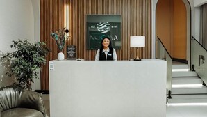 A reception desk with a modern design, a framed logo, a potted plant, and a staircase in the background. - Nooma Hotel on Frunze (Bishkek)