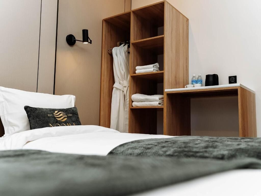 A hotel room with a bed, a wooden wardrobe, a nightstand, and a wall-mounted light fixture.