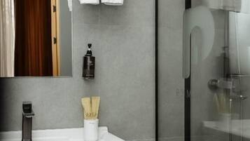 Un baño moderno con cabina de ducha de vidrio, tocador blanco con espejo y un perchero sobre el espejo.