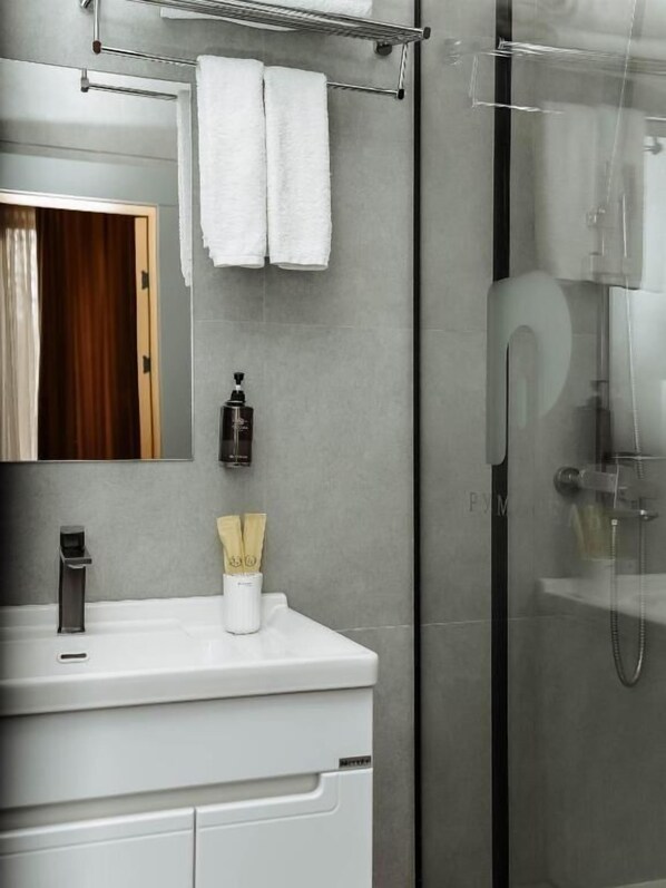 Un baño moderno con cabina de ducha de vidrio, tocador blanco con espejo y un perchero sobre el espejo.