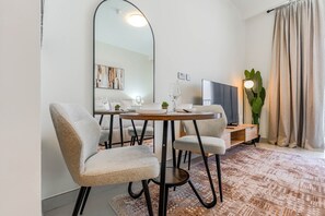 A modern dining area with a round table, two chairs, a flat-screen TV, and a large mirror. - HAVN - Studio in JVC with Pool View (Dubai)