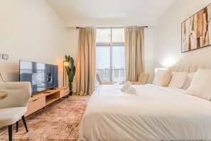 Ein Hotelzimmer mit Bett, Fernseher, Schreibtisch, Stuhl und einem Balkon mit Vorhängen.