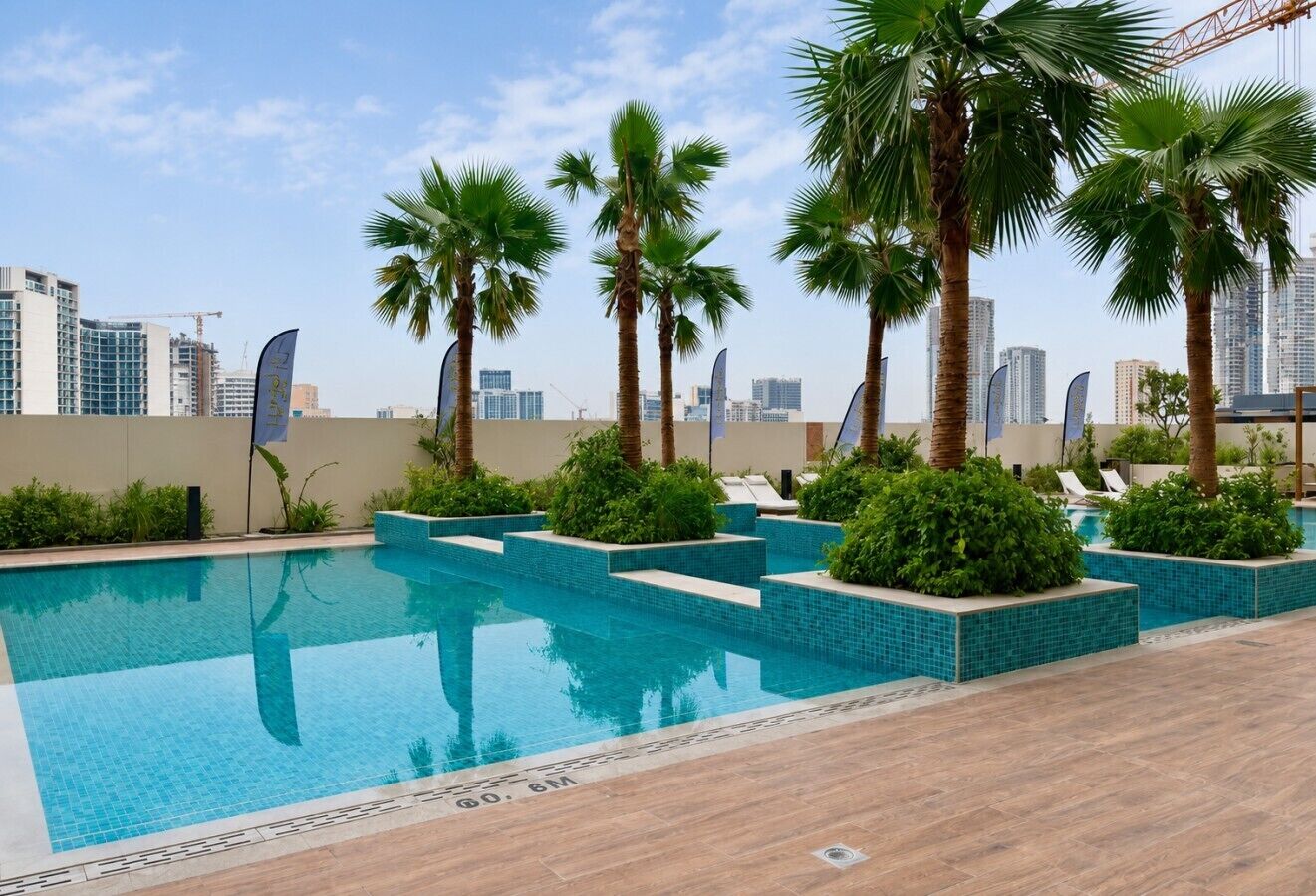 Una piscina con palmeras y sillas de descanso, rodeada de un paisaje urbano.